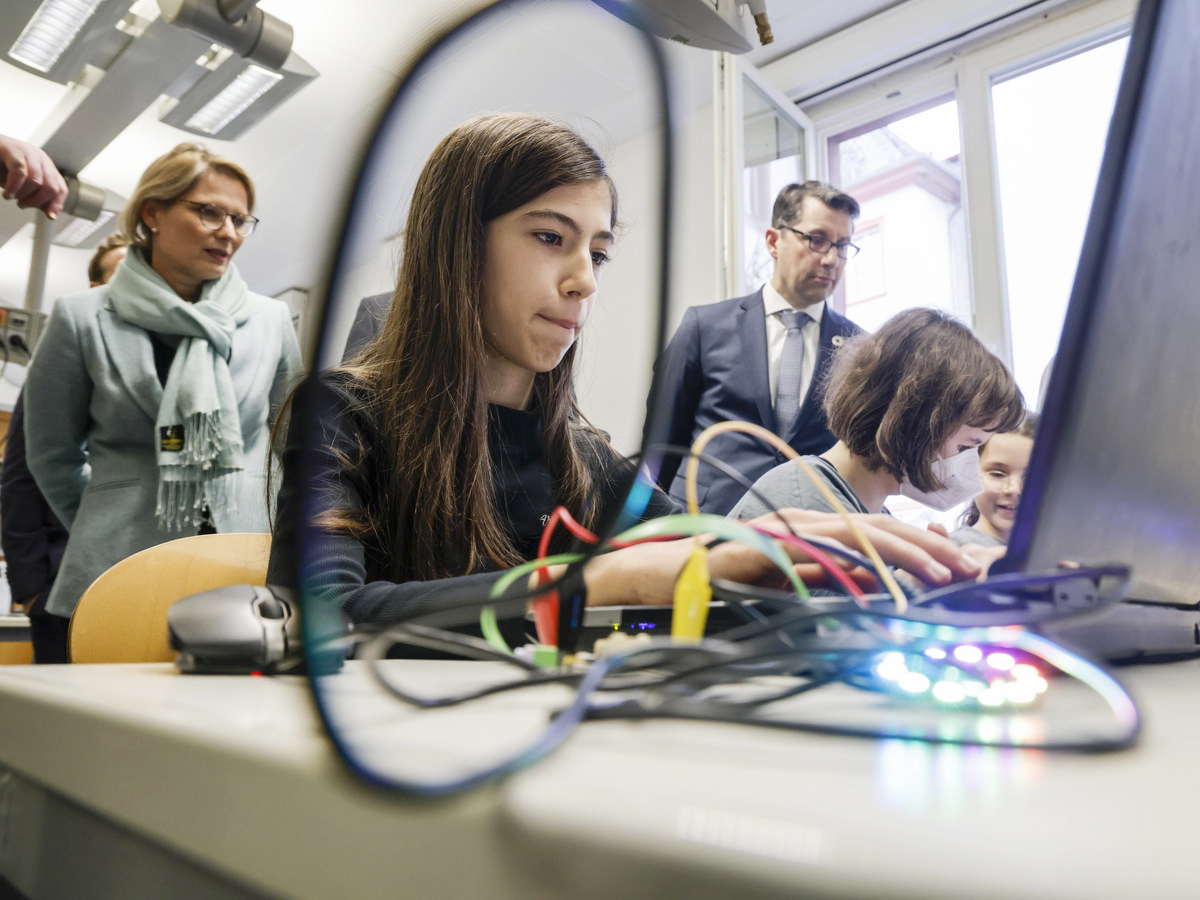 Auf dem Foto bedient eine Schülerin einen Laptop. Ministerin Hubig steht im Hintergrund.