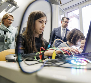 Auf dem Foto bedient eine Schülerin einen Laptop. Ministerin Hubig steht im Hintergrund.